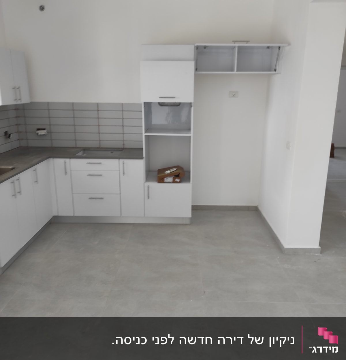 מטבח ריק עם ארונות לבנים ורצפה נקייה